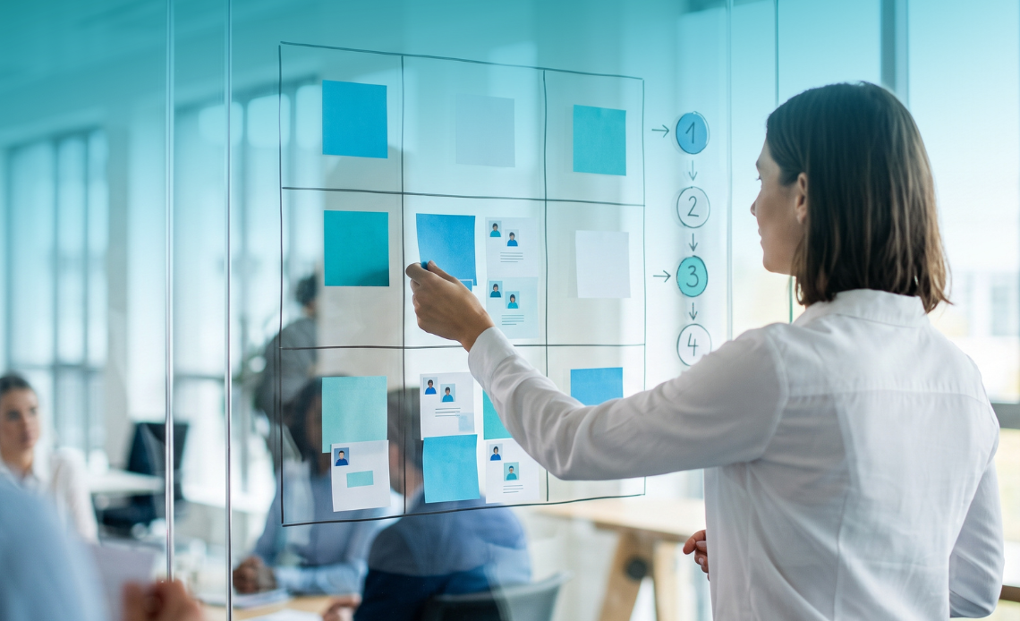 Woman placing employee profile cards on a glass board to evaluate talent using the 9 box grid method.